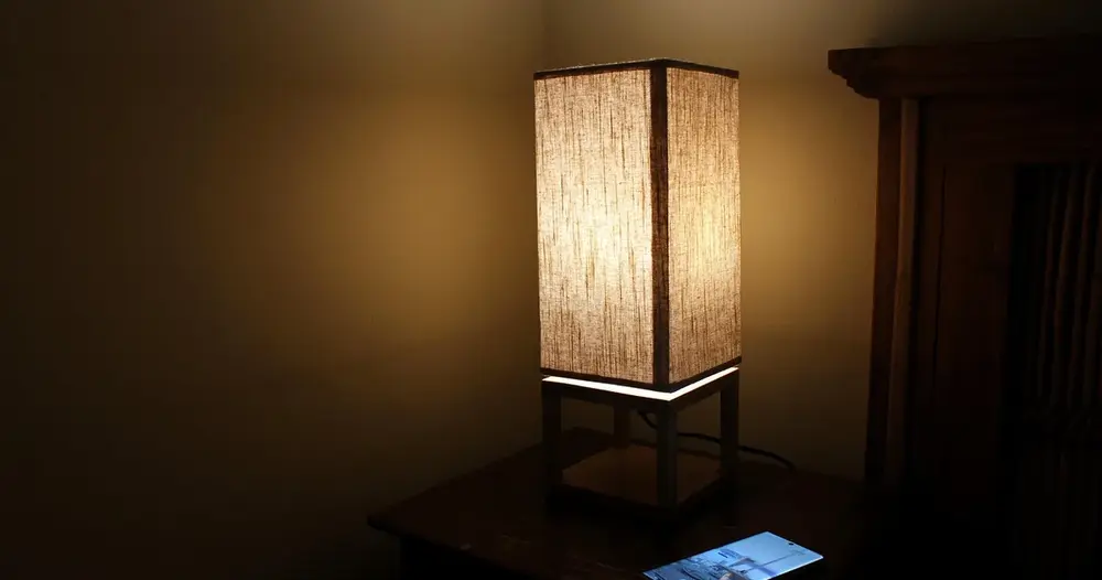 Abajur aceso sobre mesa de cabeceira em quarto escuro, cenário de quem busca como se adaptar ao CPAP à noite